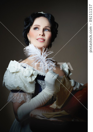 A lady with a smile in a historical costume with a feather in her hand and a letter. Design for the cover of the book. Fashion of 19th century, dress with crinoline of 1860. High quality photo A lady with a smile in a historical costume with a feather in her hand and a letter. Design for the cover of the book. Fashion of 19th century, dress with crinoline of 1860. High quality photo 89211157