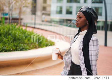 Black woman in headscarf with takeaway beverage in park 89211511