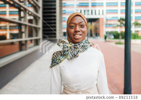 Charming black woman in Muslim headscarf standing on street Charming black woman in Muslim headscarf standing on street 89211518