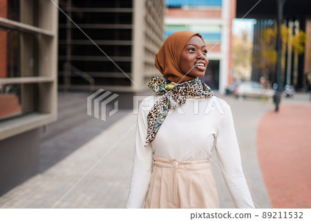 Smiling Muslim black woman in hijab standing near office building Smiling Muslim black woman in hijab standing near office building 89211532