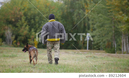A trainer walking with his trained german shepherd dog 89212604