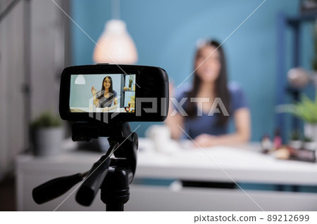 Attractive content creator greeting remote fans while recording make up tutorial advertising cosmetics product. Behind the scene of woman vlogger filming cosmetology review. Close up shot Attractive content creator greeting remote fans while recording make up tutorial advertising cosmetics product. Behind the scene of woman vlogger filming cosmetology review. Close up shot 89212699