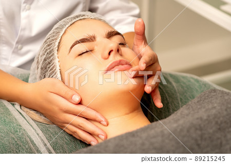 Face massage. Beautiful caucasian young white woman having a facial massage with closed eyes in a spa salon 89215245