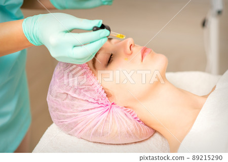 Young white woman getting acid organic retinol peel face skin with the pipette in a beauty clinic 89215290