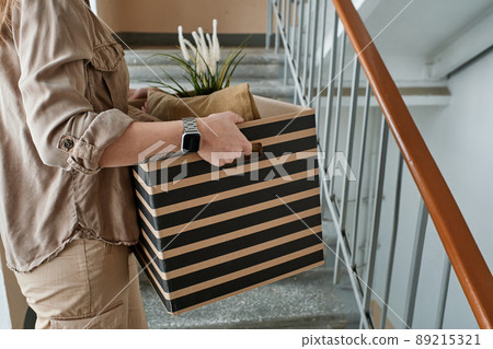 Horizontal medium section shot of unrecognizable young woman going upstairs carrying box with pillows and houseplant in it Horizontal medium section shot of unrecognizable young woman going upstairs carrying box with pillows and houseplant in it 89215321