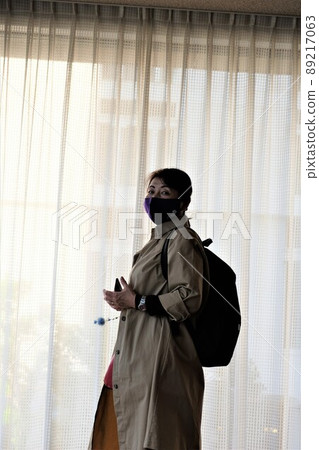 一位戴著面具的女遊客在微弱的燈光下站在蕾絲窗簾前 89217063