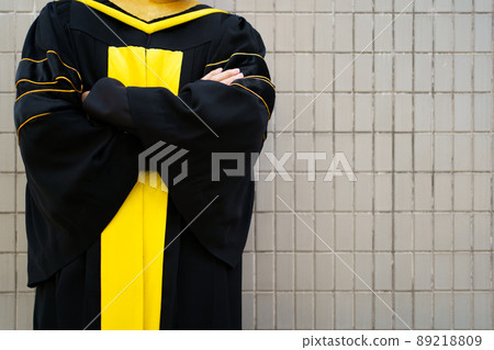 Happy Asian man in master degree gown making an arms crossing for photography against the wall with copyspace in graduate ceremony. Male graduate student in gown holding the diplomas and crossed arms. Happy Asian man in master degree gown making an arms crossing for photography against the wall with copyspace in graduate ceremony. Male graduate student in gown holding the diplomas and crossed arms. 89218809