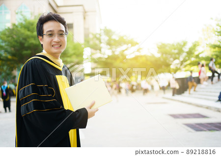 Happy Asian graduate student holding the diplomas on hand during the university graduation ceremony. Master degree student in gown suit holding a diplomas for photography. 89218816