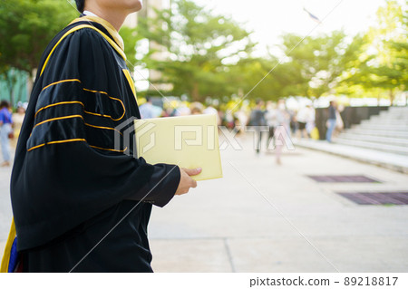 Happy Asian graduate student holding the diplomas on hand during the university graduation ceremony. Master degree student in gown suit holding a diplomas for photography. 89218817