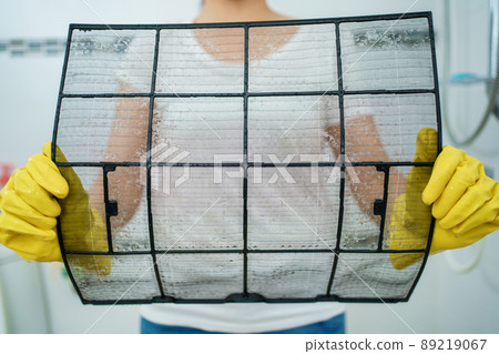 Asian woman cleaning a dirty and dusty air conditioning filter in her house. Housewife removing a dusty air conditioner filter. Asian woman cleaning a dirty and dusty air conditioning filter in her house. Housewife removing a dusty air conditioner filter. 89219067