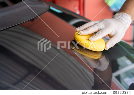 Unrecognizable Asian man cleaning and rubbing a car exterior by using a polishing sponge. Professional worker polishing a car with car wax, auto care concept. 89223584