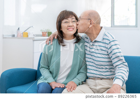 一對老夫婦坐在客廳的沙發上親吻他們的臉頰 一對老夫婦坐在客廳的沙發上親吻他們的臉頰 89226365