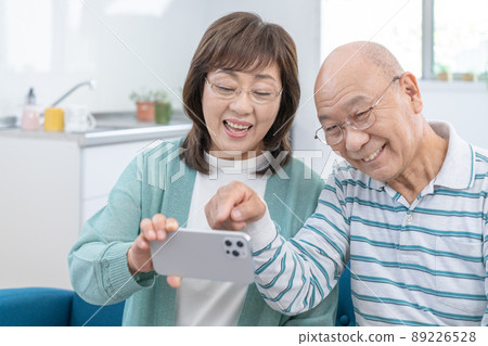 Senior couple sitting on the sofa in the living room and looking at the smartphone Senior couple sitting on the sofa in the living room and looking at the smartphone 89226528