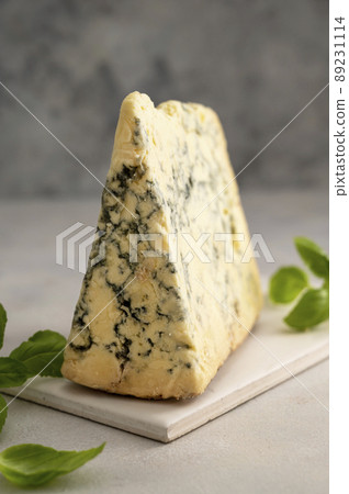 Blue cheese piece with fresh basil leaves over gray background. One triangle of cheese. 89231114