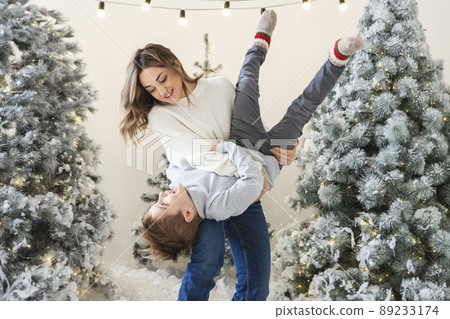 Positive young mother having fun with little boy son while standing together against tree beautiful Christmas trees decorated with xmas lights Positive young mother having fun with little boy son while standing together against tree beautiful Christmas trees decorated with xmas lights 89233174