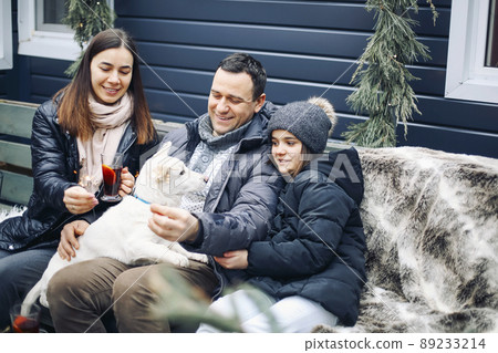 Happy young family with dog sitting on bench in house yard during winter holidays 89233214