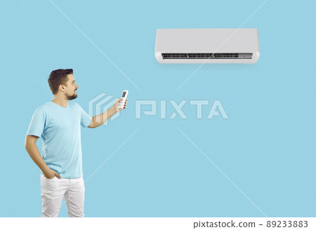 Happy young man using remote control turns on or adjusts air conditioner on light blue background. Happy young man using remote control turns on or adjusts air conditioner on light blue background. 89233883