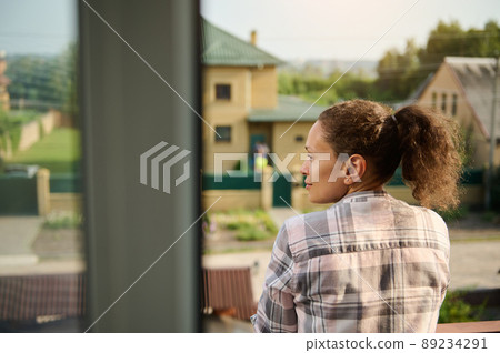 Close-up of a Hispanic woman in checkered shirt and denim shorts on her balcony Close-up of a Hispanic woman in checkered shirt and denim shorts on her balcony 89234291