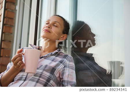 Attractive woman relaxes in the balcony of a country side house and enjoys her morning coffee Attractive woman relaxes in the balcony of a country side house and enjoys her morning coffee 89234341