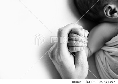 The hand of a sleeping newborn in the hand of mother and father close-up. Tiny fingers of a newborn. The family is holding hands. Studio macro photography. Concepts of family and love. Black white.  89234397