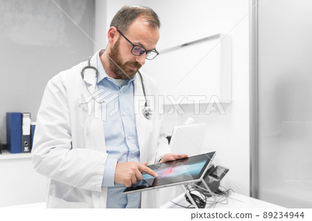 Doctor examine an x-ray image of a patient in digital tablet at doctor office. Doctor examine an x-ray image of a patient in digital tablet at doctor office. 89234944