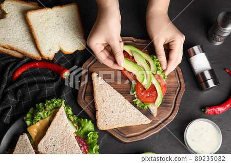 Woman making tasty sandwich with avocado at black table, top view 89235082