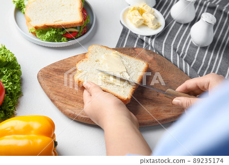 Woman spreading butter on sandwich at white table, closeup 89235174