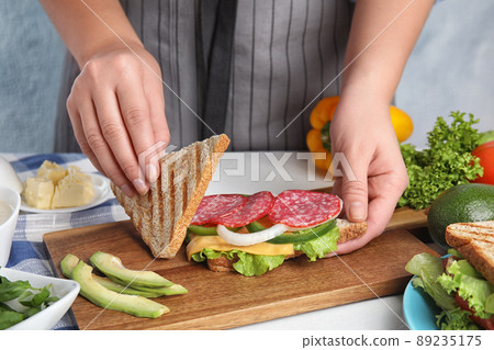 Woman making tasty sandwich with sausage at white  table, closeup 89235175