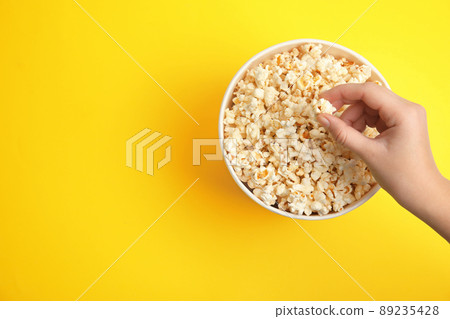 Woman taking fresh pop corn from bucket on yellow background, top view. Space for text Woman taking fresh pop corn from bucket on yellow background, top view. Space for text 89235428