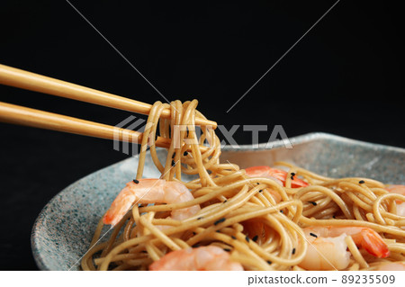 Chopsticks with tasty buckwheat noodles on black background, closeup Chopsticks with tasty buckwheat noodles on black background, closeup 89235509