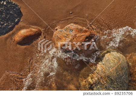 Directly Above Shot of Small Waves Rolling into Beach Dotted with Colorful Rocks and Boulders 89235706