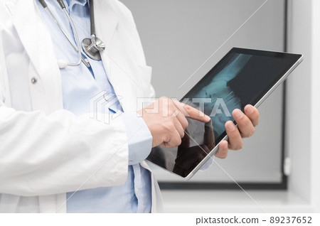 Unrecognizable Doctor is checking x-ray image at computer tablet, close up. Doctor at work in a Unrecognizable Doctor is checking x-ray image at computer tablet, close up. Doctor at work in a 89237652