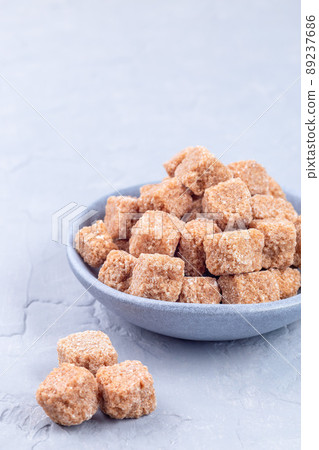 Cubes of brown sugar or cane sugar in bowl and on gray background, vertical, copy space 89237686