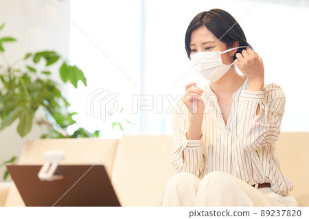 A woman holding a mask while looking at a computer camera 89237820