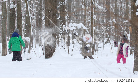 Two little girls playing with a little boy in the snow in winter forest. Throwing snowballs Two little girls playing with a little boy in the snow in winter forest. Throwing snowballs 89241813