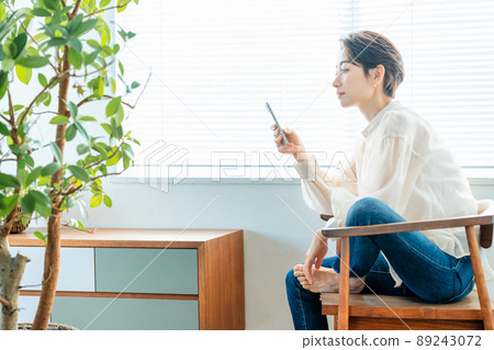 Middle-aged woman using a smartphone by a bright window 89243072