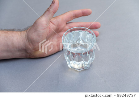 A man's hand intends to take a glass of water. A glass of clear drinking water against a gray background. 89249757