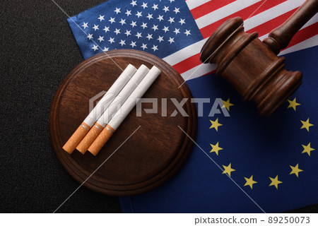 Cigarettes and Judge gavel on the USA and EU flag. Illegal sale of tobacco products. Smuggling of illegal goods. Cigarettes and Judge gavel on the USA and EU flag. Illegal sale of tobacco products. Smuggling of illegal goods. 89250073