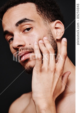 Portrait of young metrosexual man applying cream on his face and looking at camera 89250848