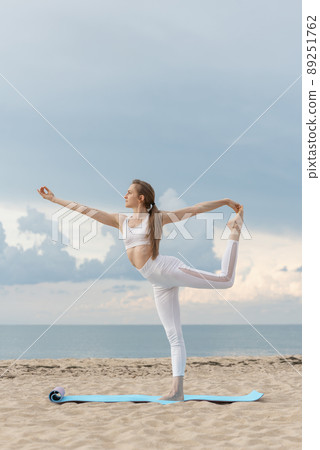 Young beautiful sportwoman practicing yoga in Natarajasana on sea background. Woman is making yoga on the beach. 89251762