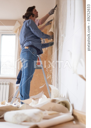 Young couple removing old wallpaper from walls preparing for flat renovation. 89252633