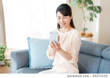 Middle woman operating a smartphone in the room Middle woman operating a smartphone in the room 89253339