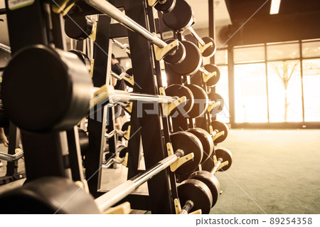 Close up row of barbells dumbbells in modern sports club with soft light. Close up row of barbells dumbbells in modern sports club with soft light. 89254358