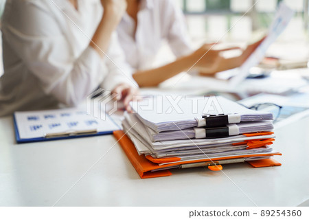 Close up at documents of unfinished documents on office desk with blurry female office worker working as background. 89254360