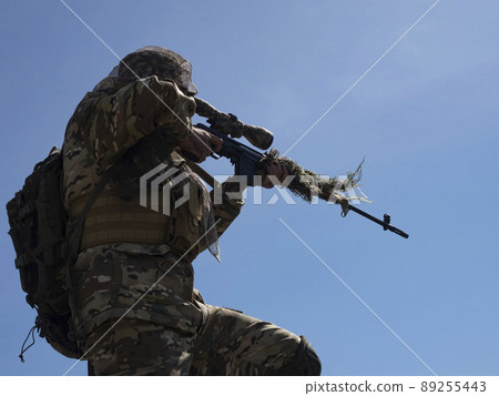 A professional special forces sniper during a special operation - aims at the enemy against the blue sky. A professional special forces sniper during a special operation - aims at the enemy against the blue sky. 89255443
