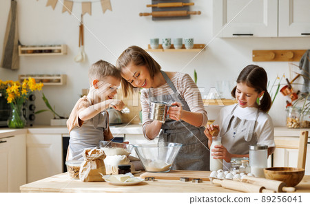 Happy woman and cute children cooking together in kitchen Happy woman and cute children cooking together in kitchen 89256041