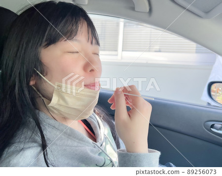 A woman performing a PCR test in a car using a cotton swab 89256073