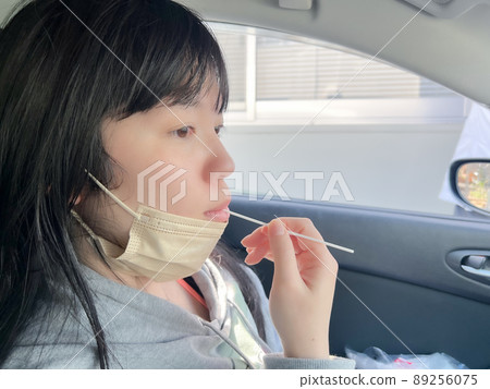 A woman performing a PCR test in a car using a cotton swab 89256075