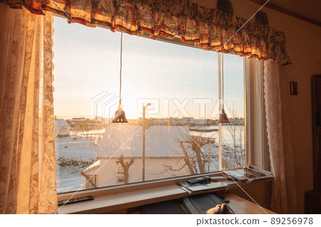 View from curtain window with sunset over snowy village on coastline in winter View from curtain window with sunset over snowy village on coastline in winter 89256978