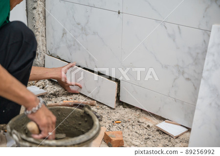 Male tiler using trowel laying marble tile with cement in bathroom. Housing development, improvement renovation 89256992